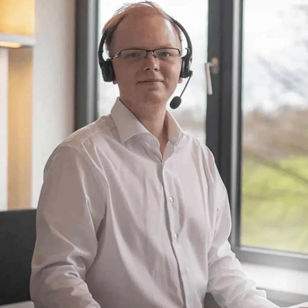 Porträt eines Mitarbeiters mit Headset auf dem Kopf und weißem Hemd.