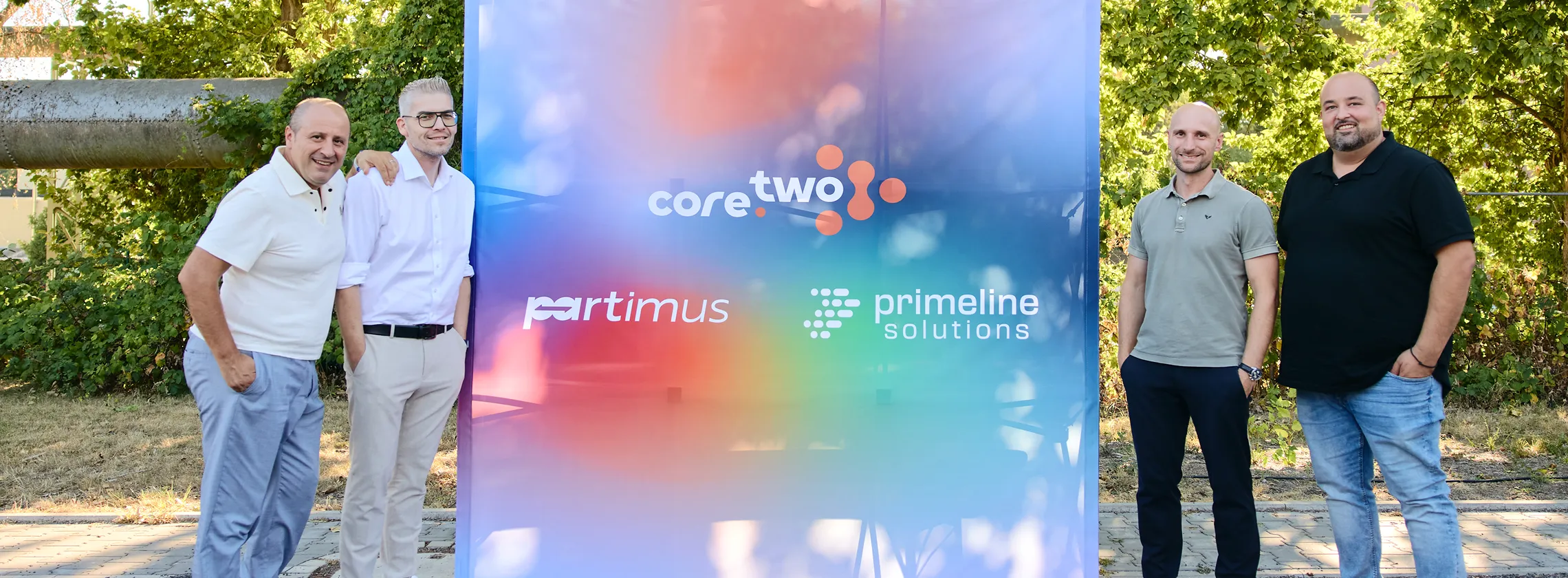 Die Geschäftsführer der core.two Unternehmensgruppe neben einem Banner mit den drei Logos der Gruppe
